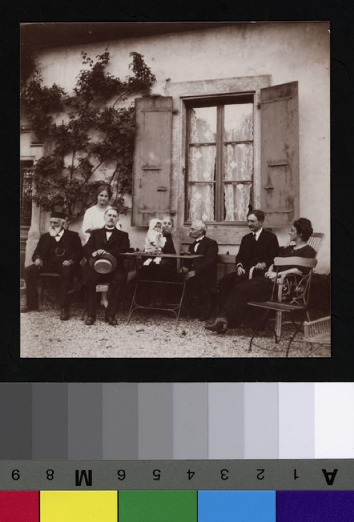 Portrait du Prof. Dr. César Roux et de sa famille, devant leur maison, à Mont-la-Ville. Ils posent assis, à l'extérieur, autour d'une table de jardin. De gauche à droite: M. Louis Roux,_x000D_
Hélène Roux,_x000D_
Dr Bégoune,_x000D_
Mme Roux avec Anne Picot dans ses bras…