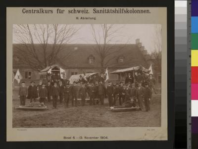 Portraits des participants par équipes au cours d'aides sanitaires qui eut lieu à Bâle du 6 au 13 novembre 1904. Les portraiturés sont debout, assis sur des charrettes ou couchés sur des brancards sur un champ devant une grande bâtisse .