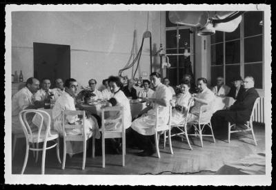 Groupe de médecins attablés dans une des salles de traitement médical de l'Hôpital cantonal, comme le laissent supposer les différents appareils et machines. A l'extrême droite de la table, à côté de la dame avec le chapeau, le Dr. Alfred Rosselet, ave…