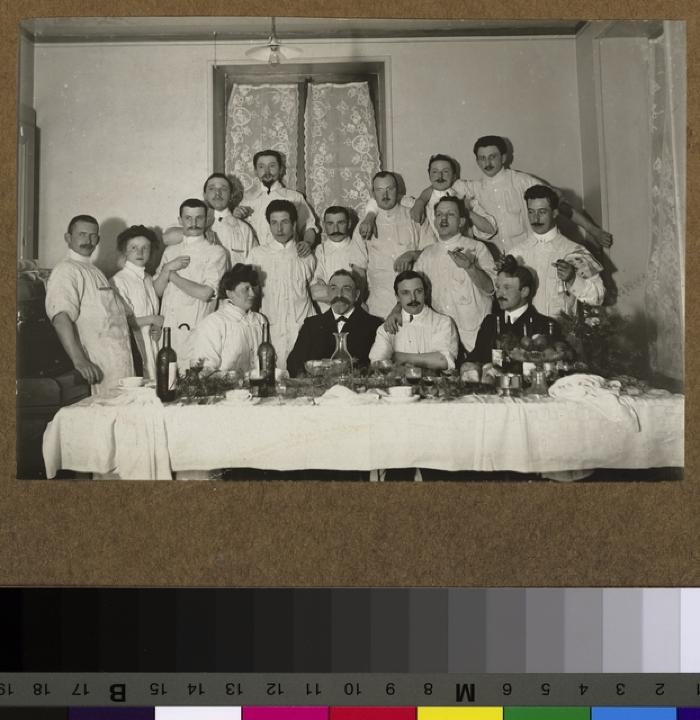 Groupe de médecins attablés dans probablement le réfectoire des médecins de l'Hôpital cantonal, vraisemblablement à l'occasion des fêtes de Noël.
