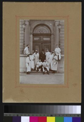 Portrait d'un groupe de médecins et d'assistants devant l'entrée principal de l'Hôpital cantonal. Le docteur Paul Narbel est débout, deuxième depuis la gauche, une pipe à la bouche.