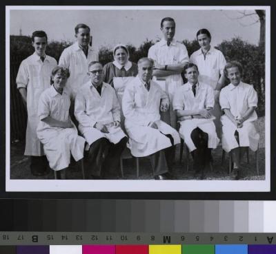 Portrait du Professeur Lucien Pautrier, assis au centre avec une cigarette, entouré de ses collaborateurs (des médecins et une infirmière).