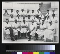 Portrait du Professeur Pierre Decker (3e au premier rang, à partir de la droite) entouré d'un groupe de jeunes médecins. Ils sont dans le grand auditoire de l'annexe chirurgicale de l'Hôpital cantonal.