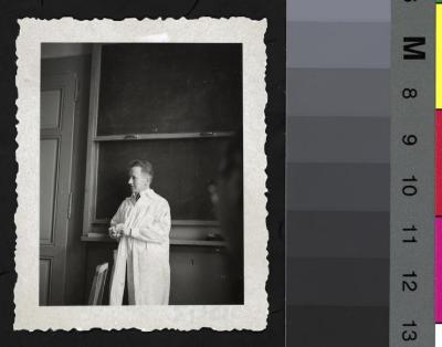 Portrait en pied du Prof. Amsler Marc dans une salle de cours, habillé avec une blouse blanche de médecin. Derrière lui, le tableau noir.