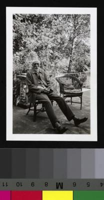 Portrait du Dr Eugène Olivier, âgé, assis sur une chaise de jardin en osier. Derrière lui, de la végétation.