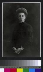 Portrait en pied de la doctoresse Charlotte Olivier-von Mayer (1864-1945). Elle porte une robe noire avec un ourlet blanc au col et aux poignets.