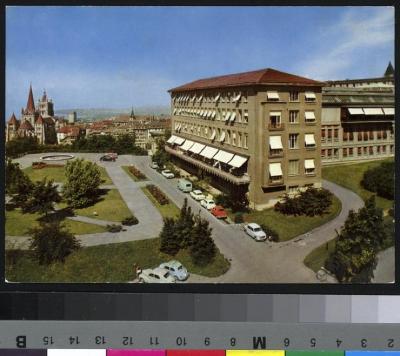 Vue sur le pavillon chirurgical de l'hôpital cantonal. Au premier plan, on voit le jardin et le parking où sont parquées des voitures.