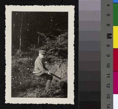 Portrait assis du Prof. Dr. César Roux en tenue de chasseur avec un fusil, au milieu de la forêt. A la ceinture, une corne de chasse. A l'angle droit de l'image, un chien.