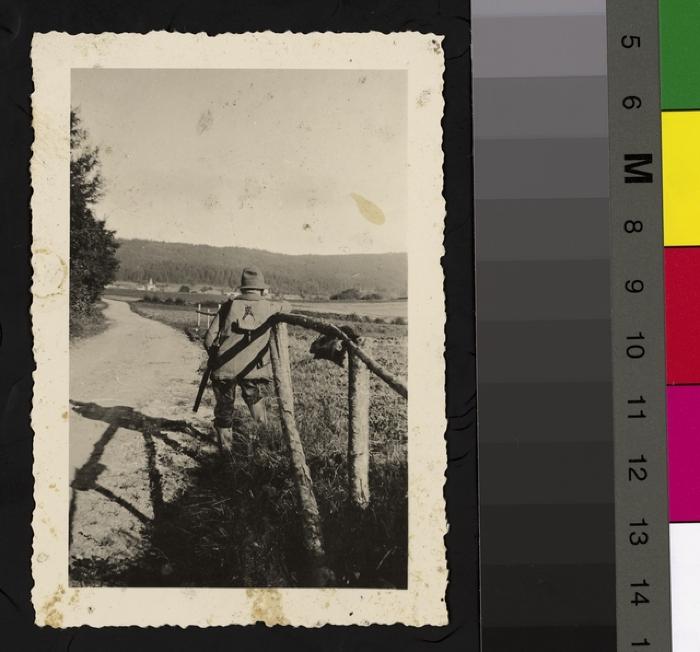 Portrait de dos du Prof. Dr. César Roux en tenue de chasseur avec un fusil. Il est appuyé à une clôture en bois.